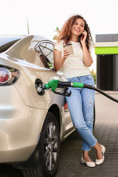 African-American woman talking by phone while filling up car tank at gas station - Photo, Image