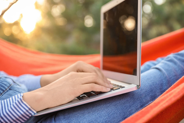 Beautiful young woman with laptop relaxing in hammock outdoors, closeup - Foto, imagen