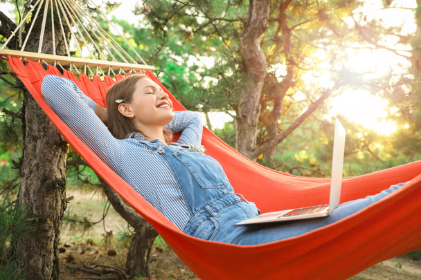 Belle jeune femme avec ordinateur portable relaxant dans l'hamac en plein air - Photo, image