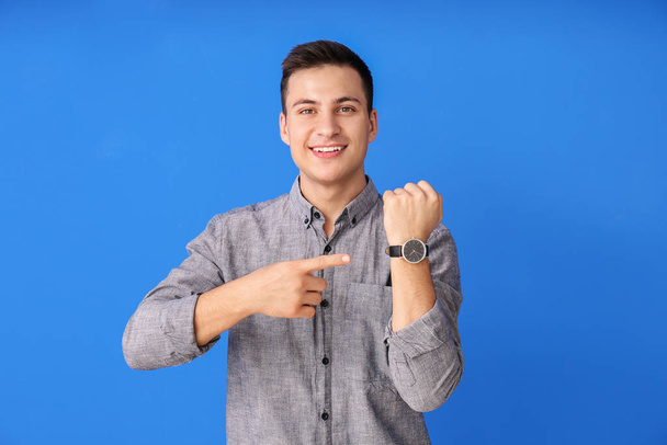 Hombre joven con reloj de pulsera sobre fondo de color - Foto, Imagen