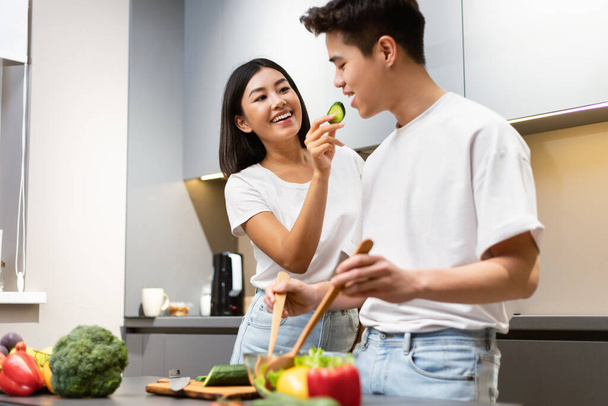 Japanese Couple Tasting Food While Cooking Dinner Together In Kitchen - Fotografie, Obrázek