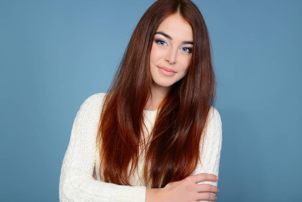 Young attractive woman's portrait, beautiful girl with long hair and white pullover, studio shot over blue background - Zdjęcie, obraz