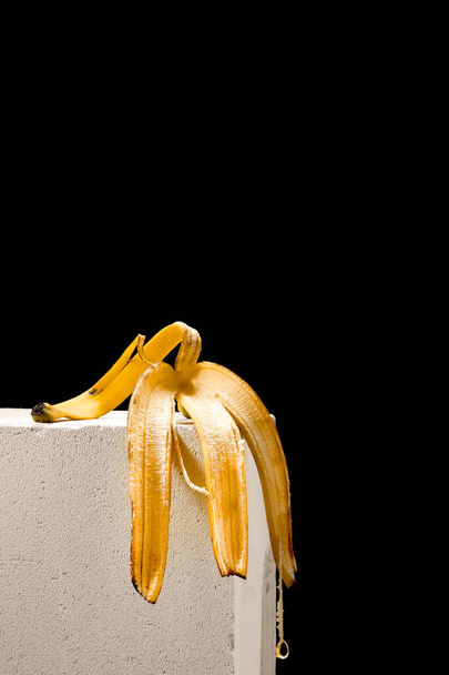 Banana skin on a white block stand, black background. Poster concept or idea - Photo, Image