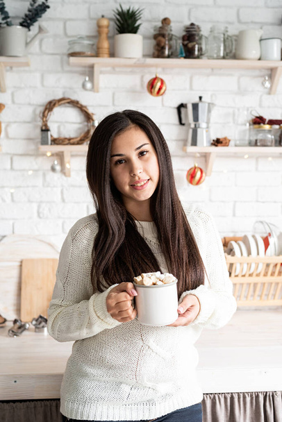 Christmas and New Year. Brunette woman holding a cup of marshmallow cocoa in the kitchen - Fotografie, Obrázek