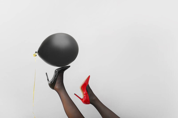 Female legs in high-heeled shoes and with black air balloon on grey background - Fotoğraf, Görsel