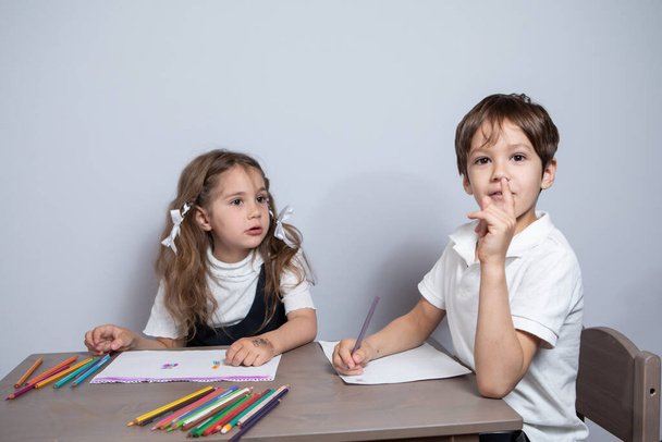 Дівчинка і хлопчик сидять за столом і тримають олівці. Вони малюють
. - Фото, зображення