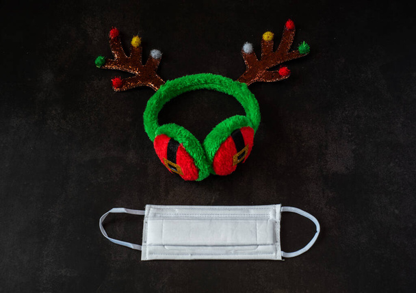 Medizinische Maske mit Weihnachten Spielzeug Regenhörner auf dunklem Hintergrund, zu Hause bleiben Neujahr - Foto, Bild