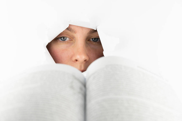 Una mujer lee un libro a través de un agujero en el papel blanco. Estudio, conciencia, cognición. Espacio libre para texto. - Foto, Imagen