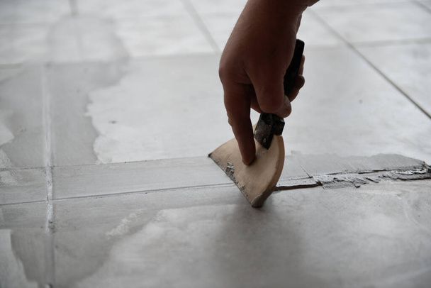 Tiler laying the ceramic tile on the floor. Professional worker makes renovation. Construction. Hands of the tiler. Home renovation and building new house - Фото, зображення
