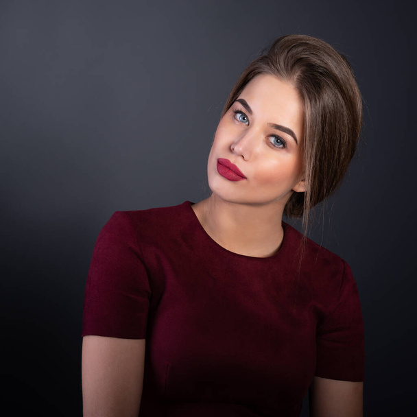 Portrait of attractive young woman over gray background. Amazing girl with perfect makeup wearing elegant deep red dress. Beauty and fashion - Φωτογραφία, εικόνα