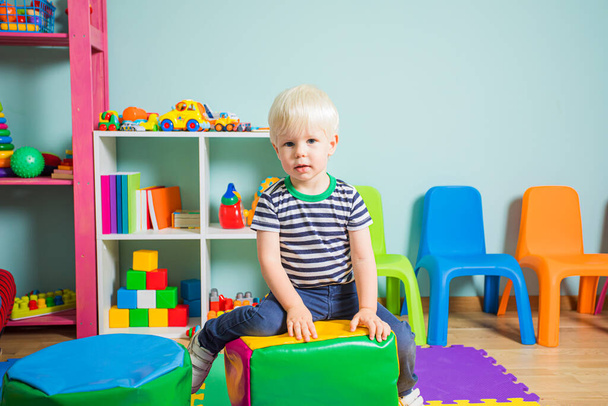 The toddler boy is sitting on a pouf in the kindergarten - Photo, Image