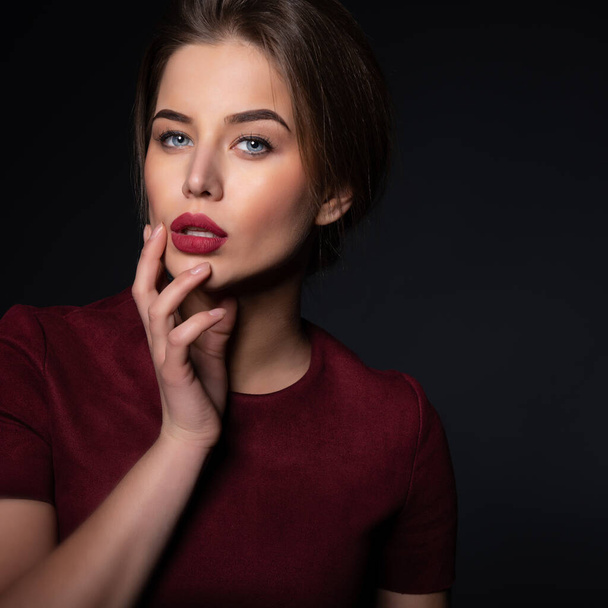 Portrait of attractive young woman over black background. Amazing girl with perfect makeup wearing elegant deep red dress. Beauty and fashion - Foto, immagini