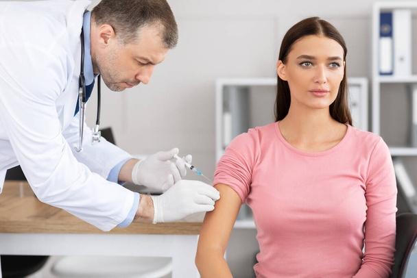 Medico di sesso maschile che effettua la vaccinazione contro il coronavirus alla giovane donna - Foto, immagini