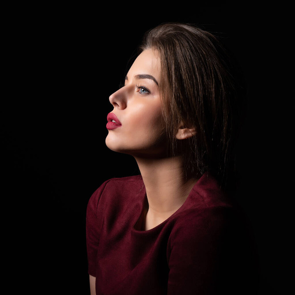Portrait of attractive young woman over black background. Amazing girl with perfect makeup wearing elegant deep red dress. Beauty and fashion - 写真・画像