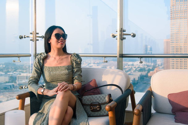 Kobieta pije drinka i podziwia widok na Dubaj w Zjednoczonych Emiratach Arabskich z góry o zachodzie słońca - Zdjęcie, obraz