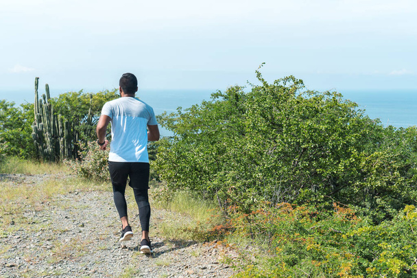 A young African-American man running down the mountain, the man goes out on his back and wears sportswear - Photo, Image