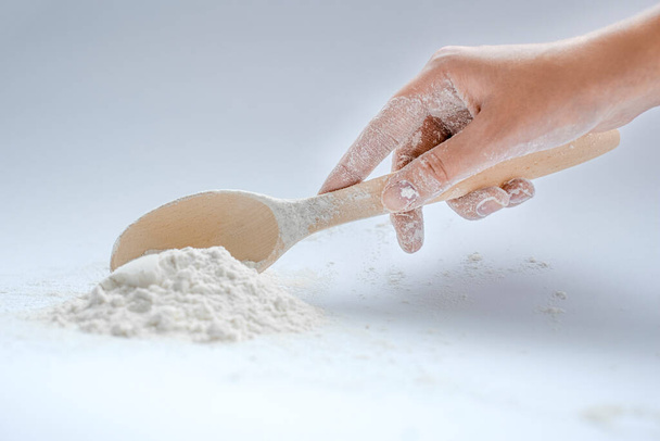 the girl's hand holds a wooden spoon with whole grain flour on a light background close-up. ingredients for making a pie. healthy foods - Φωτογραφία, εικόνα
