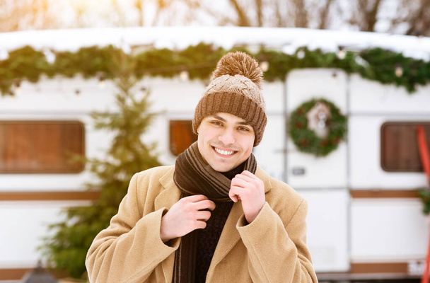 Красивый молодой человек позирует на открытом воздухе рядом с современным кемперваном в зимний день - Фото, изображение