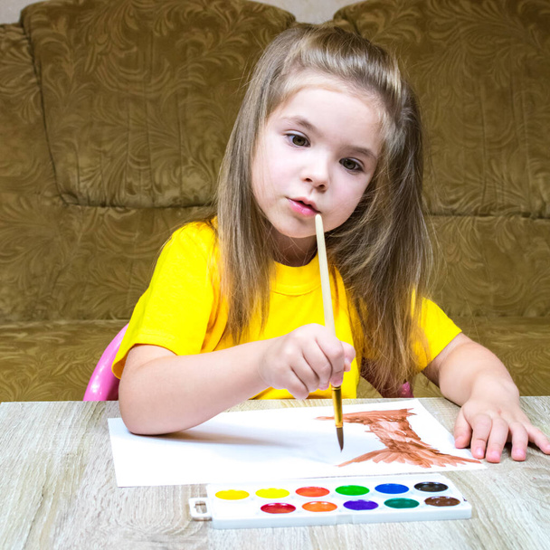 A little girl in a yellow T-shirt draws a tree trunk with watercolors. - Photo, Image