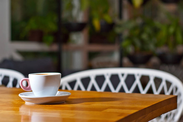 Weiße Kaffeetasse auf einem Holzbrett. Verschwommenes Bar-Interieur im Hintergrund. Freier Platz in der Nähe des Kaffees. - Foto, Bild