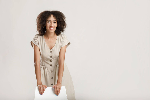 Neşeli, kıvırcık, Afro-Amerikan genç kadın portresi. Sandalyeye yaslanmış kameraya bakıyor ve gülümsüyor. - Fotoğraf, Görsel