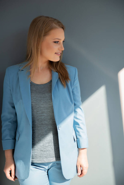 Beautiful fashion woman wearing light blue summer suit posing indoor over gray wall, natural light - Fotoğraf, Görsel