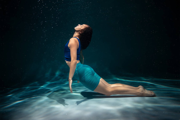 The girl is engaged in yoga under the water in sports clothes. Asanas and Meditation - Zdjęcie, obraz