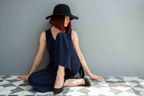 Fashion woman wearing deep blue clothes and black hat posing indoor  - Valokuva, kuva