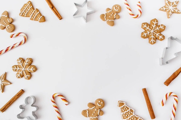 Christmas, winter, new year composition. Christmas frame made of cinnamon sticks, candies, gingerbread on white background. Flat lay, top view, copy space - 写真・画像