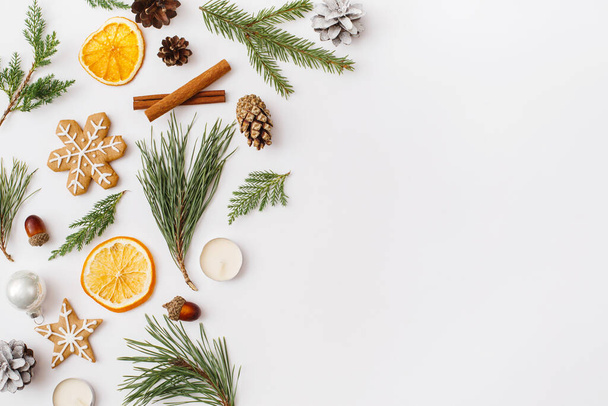 Christmas, winter, new year composition. Fir tree branches, pine cone, dried oranges, cinnamon sticks, gingerbread, candles on white background. Flat lay, top view, copy space - Foto, afbeelding