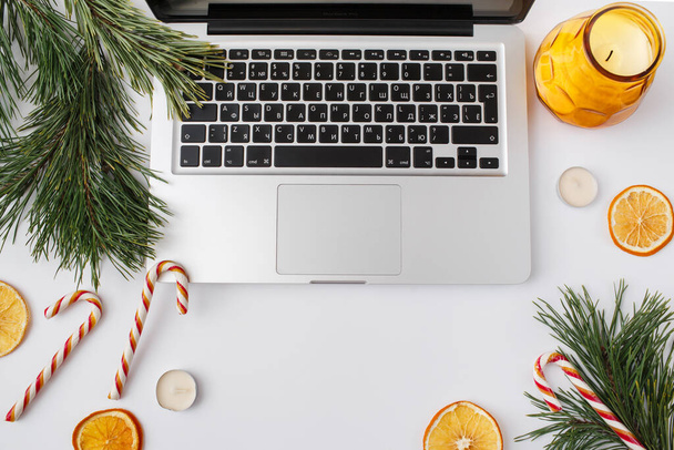 Christmas, winter, new year composition. Home office desk workspace with Fir tree branches, dried oranges, candies, candles on white background. Flat lay, top view - Foto, Bild
