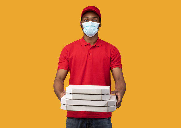 Livreur noir dans un masque médical tenant des boîtes à pizza - Photo, image