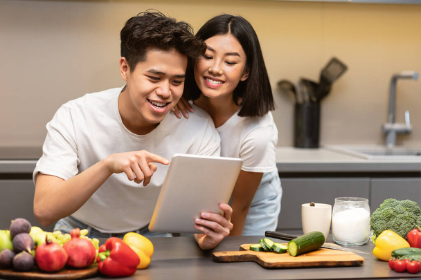 Esposo y esposa coreanos cocinando usando tableta digital en la cocina - Foto, imagen
