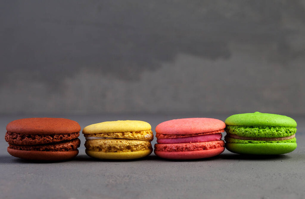 Multi-colored macaroons cakes in a row on a dark gray concrete background. Macaroons on a gray concrete background. Cakes on top of each other. Space for text, copy space. - Photo, Image
