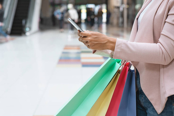 Aplicación de compras. Mujer negra llevando bolsas de compras y usando Smartphone en el centro comercial - Foto, imagen
