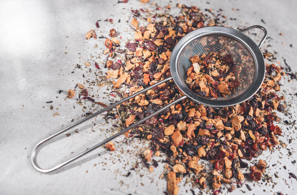 Fruit tea of dried flowers petals and dry berries with strainer or infuser - filter on gray table - Foto, Bild
