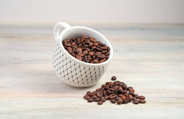 Чашка кофе с жареными кофейными зёрнами на светлом деревянном фоне. - Фото, изображение