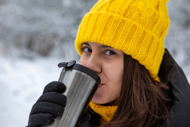 Улыбающаяся женщина в зимнем наряде пьет разогретый напиток из заполняемого места для копирования кружки - Фото, изображение