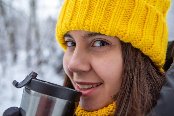 usmívající se žena v zimním oblečení pití zahřát nápoj z plnitelný hrnek kopírovat prostor - Fotografie, Obrázek