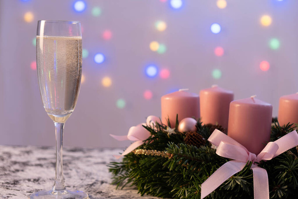 A glass of champagne stands on the table, next to a Christmas wreath in the back of a garland on a white background - Valokuva, kuva