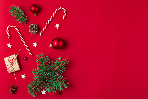 Kerstcompositie. Cadeaus, sparren takken, snoep, decoraties op rode achtergrond. Kerstmis, winter, nieuwjaarsconcept. Vlakke lay, bovenaanzicht met kopieerruimte - Foto, afbeelding
