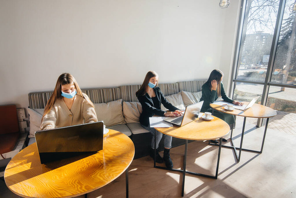 A group of masked girls keep a social distance in a cafe when working on laptops. - 写真・画像