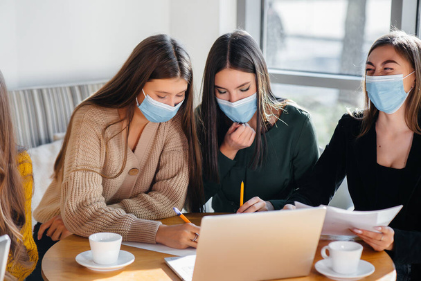 A group of girls in masks sit in a cafe and work on laptops. Teaching students. - Fotografie, Obrázek