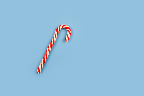 Bastón de caramelo duro de menta rayado en colores navideños sobre fondo azul. Primer plano.. - Foto, Imagen