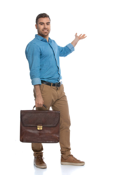 Yakışıklı, sıradan bir adam bir şey sunuyor ve elinde beyaz arka planda bir çanta tutuyor. - Fotoğraf, Görsel