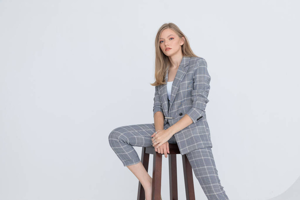 seated elegant businesswoman in gray checkered suit holding hands and confidently posing on light gray background in studio - Foto, afbeelding