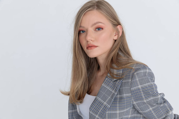 close up of beautiful young girl wearing gray checkered suit and posing on light gray background in studio - Fotografie, Obrázek