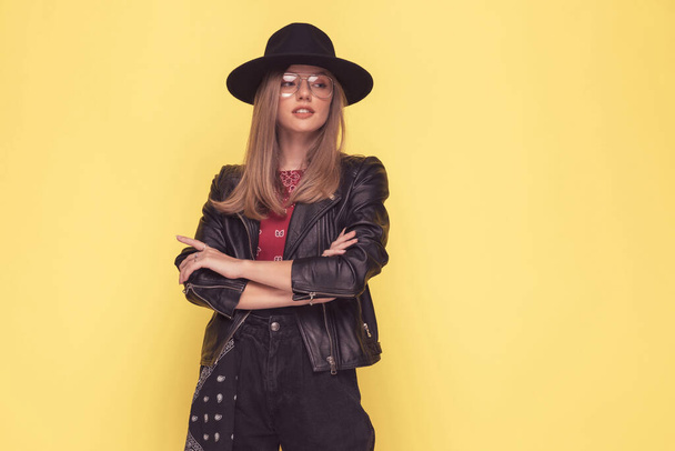 attractive fashion model crossing her arms, looking away and wearing a cool hat, leather jacket and eyeglasses - Photo, Image