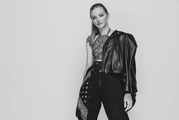 fashion young girl with ponytail wearing leather jacket on shoulder, standing in a cool position and posing on black and white background in studio - Photo, Image