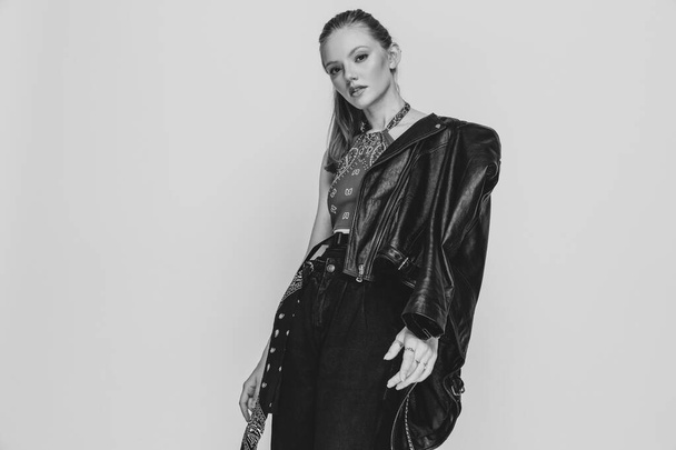 ブロンド女性モデル身に着けている革のジャケット肩と自信を持って上の黒と白の背景でスタジオ - 写真・画像